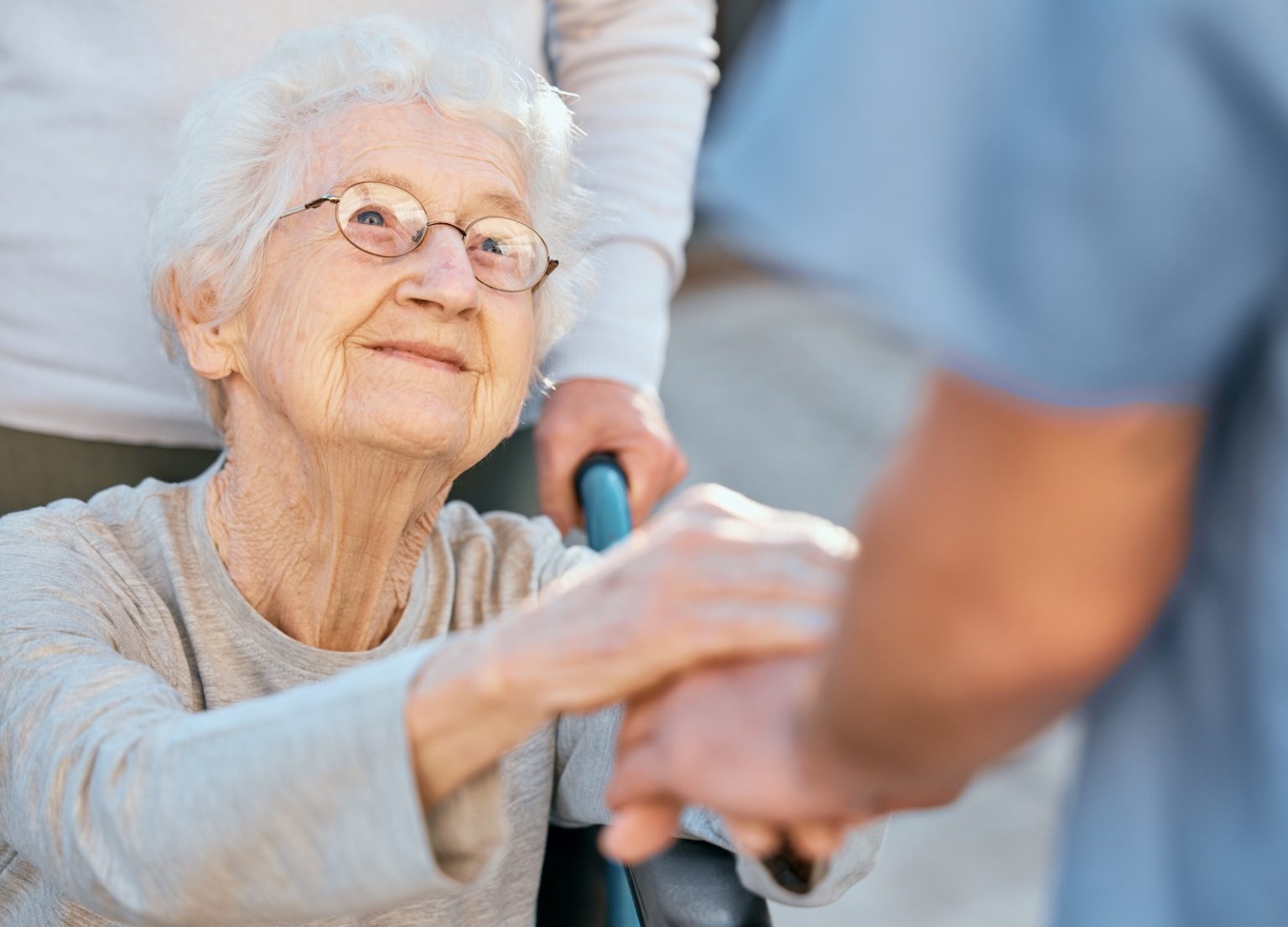 Holding hands, caregiver and senior woman in wheelchair for support outdoor in retirement home. Love, trust and healthcare nurse or medical wellness doctor for disability patient with kindness.