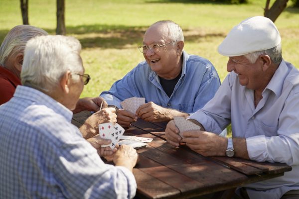 Active retirement, old people and seniors free time, group of four elderly men having fun and playing cards game at park. Waist up